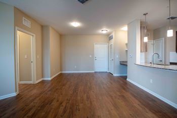 An empty living room with wood flooring and a kitchen